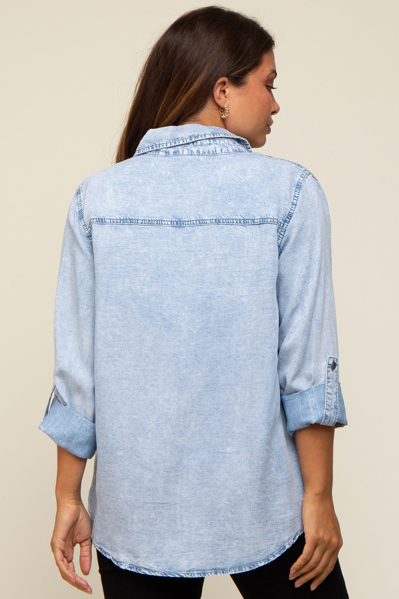 woman wearing a light blue maternity denim shirt, shown from the back with rolled-up sleeves