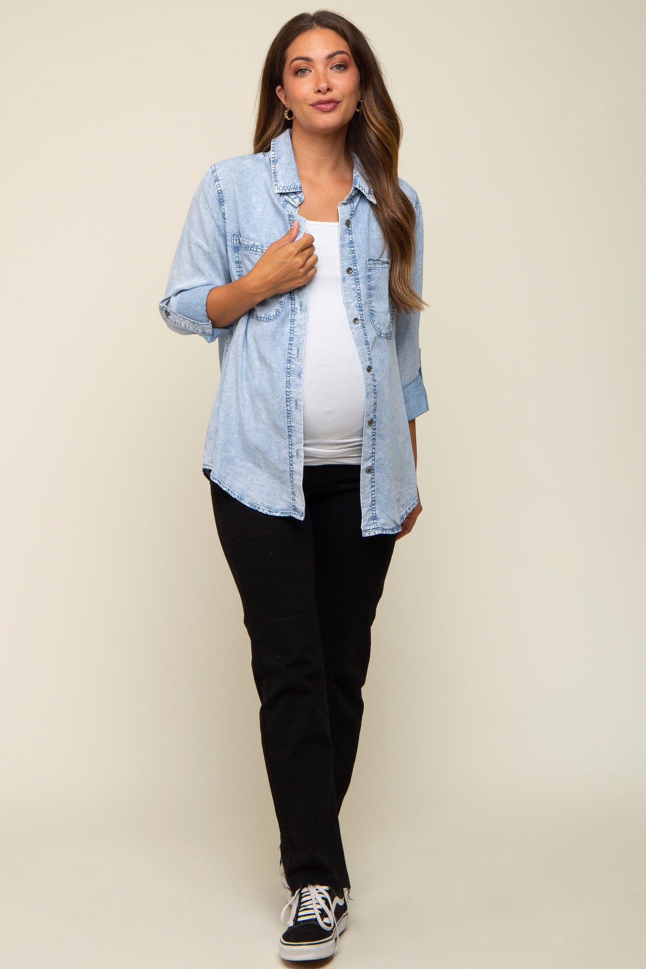 woman wearing a light blue maternity denim button-up shirt and black pants, showcasing her baby bump