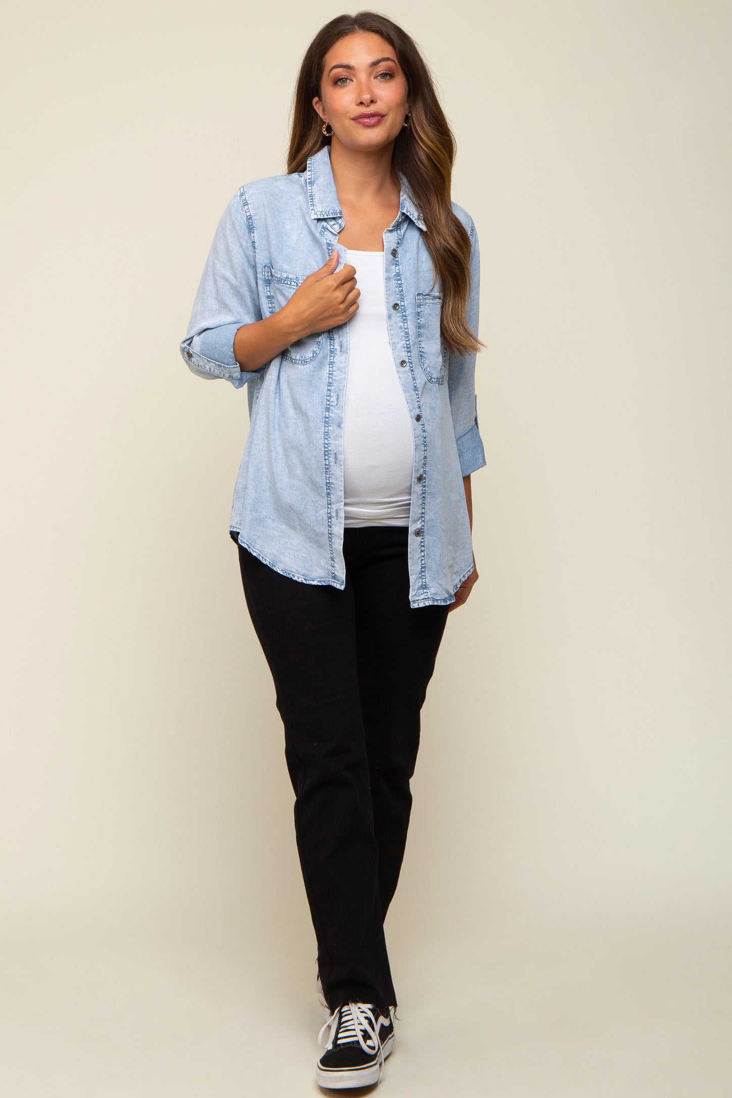 woman wearing a light blue maternity denim button-up shirt and black pants, showcasing her baby bump