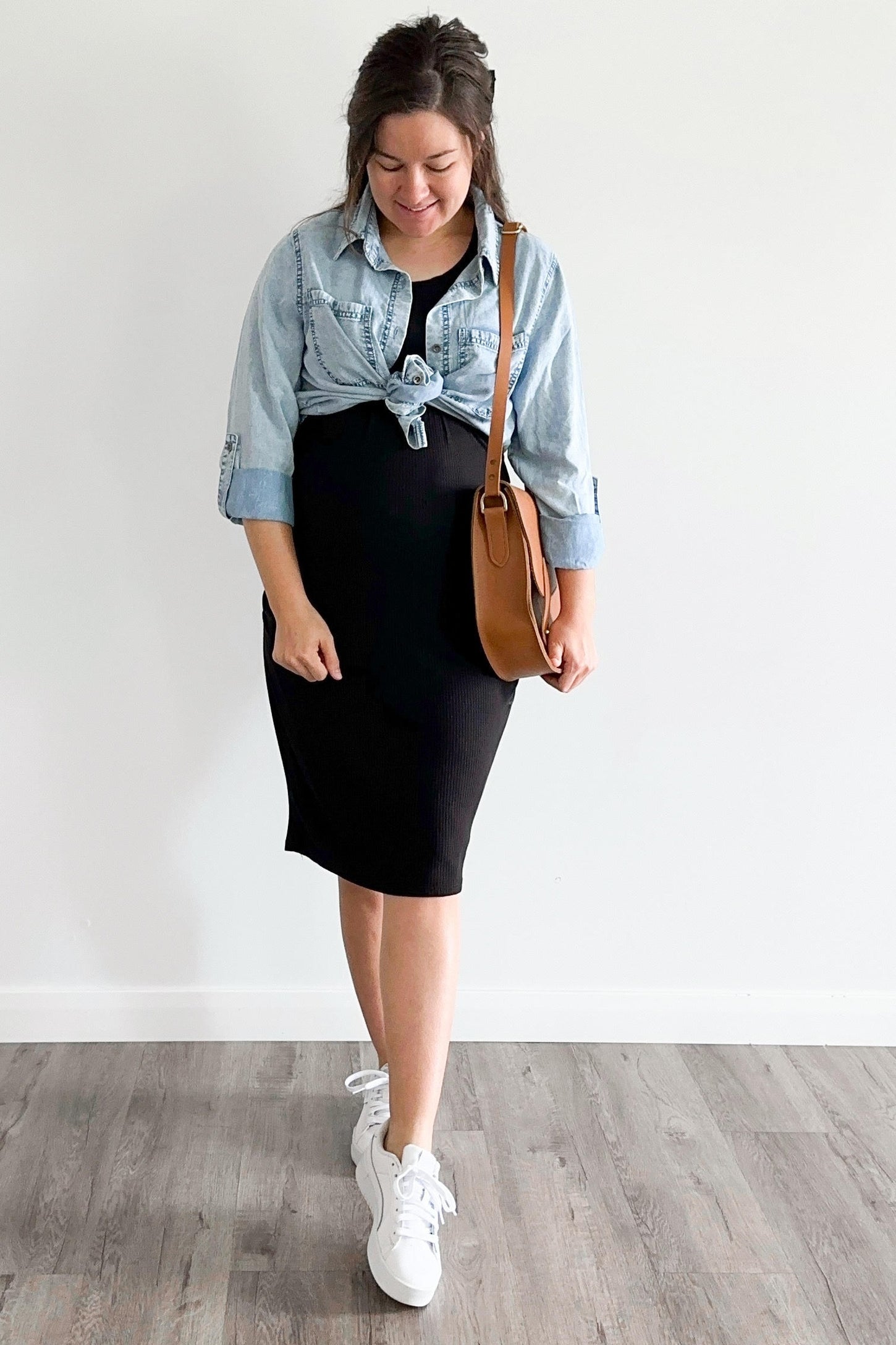 woman wearing a black maternity dress with a knotted denim shirt and carrying a brown crossbody bag