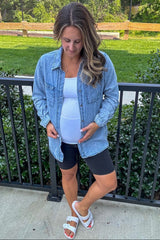 woman wearing a light blue denim button-up shirt over a white tank top, black maternity shorts, and showing her baby bump