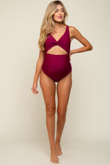 woman wearing a burgundy maternity swimsuit with a cutout detail and adjustable straps, showcasing her baby bump