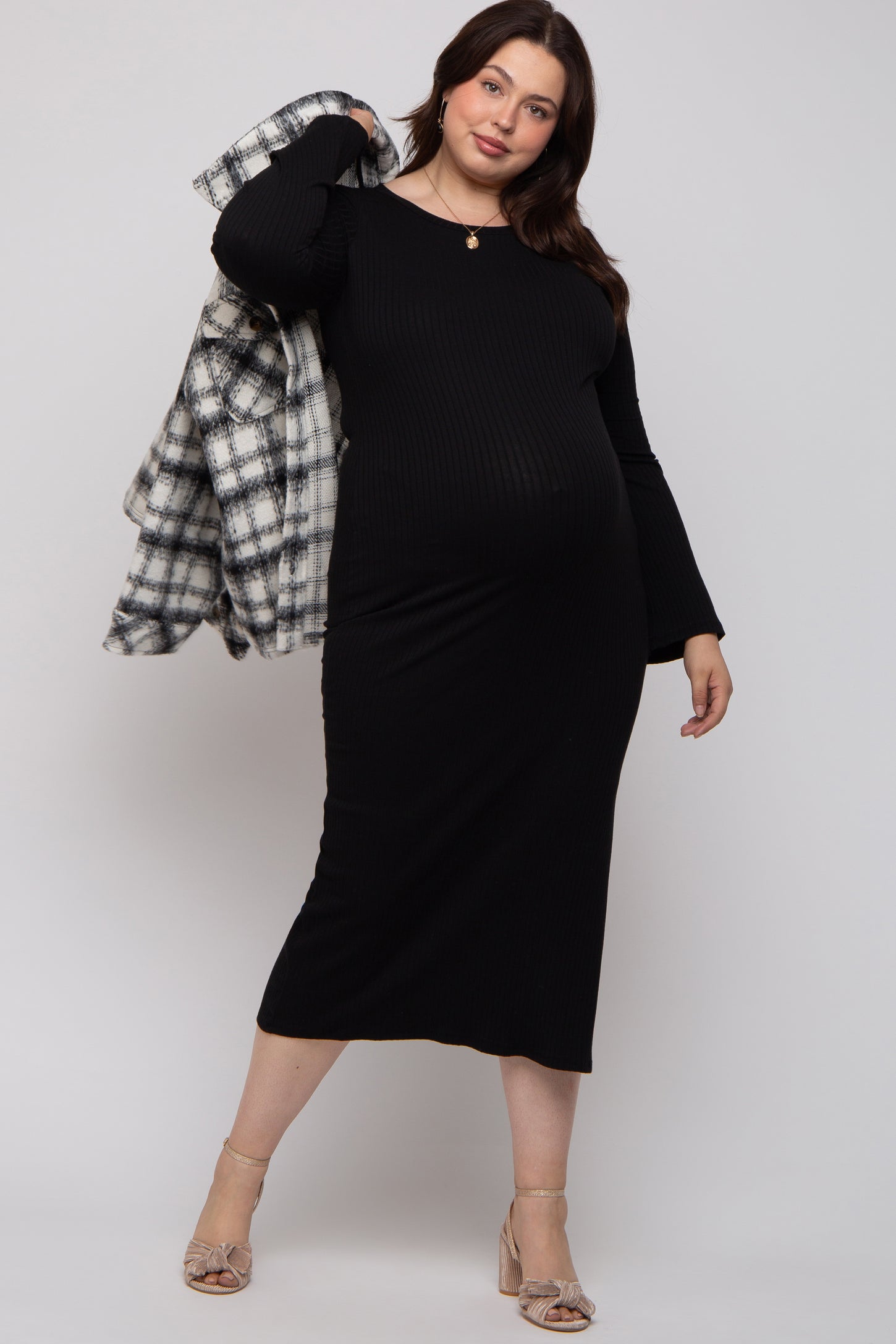 woman wearing a black ribbed long sleeve maternity dress and holding a plaid jacket, showing her baby bump