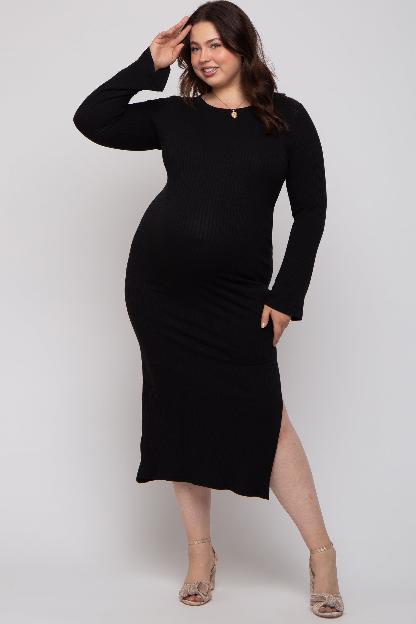 woman wearing a black ribbed maternity plus dress with long sleeves and a side slit, showcasing her baby bump
