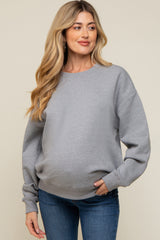 woman wearing a gray oversized sweatshirt, styled for maternity wear, with a visible baby bump and paired with blue jeans