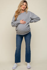 woman wearing a gray oversized sweatshirt with a visible baby bump and blue flared maternity jeans