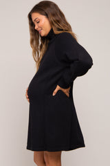 woman wearing a black maternity sweater dress with side pockets and a visible baby bump