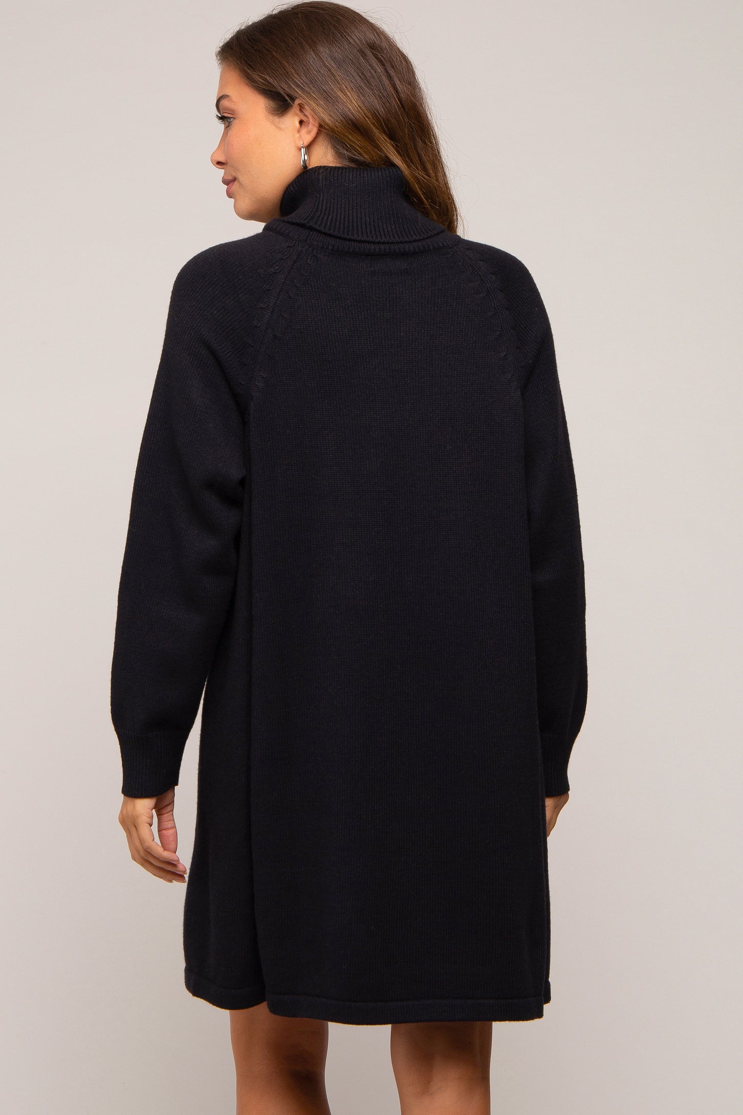 woman wearing a black oversized maternity sweater dress with a high collar and long sleeves, showing the back view