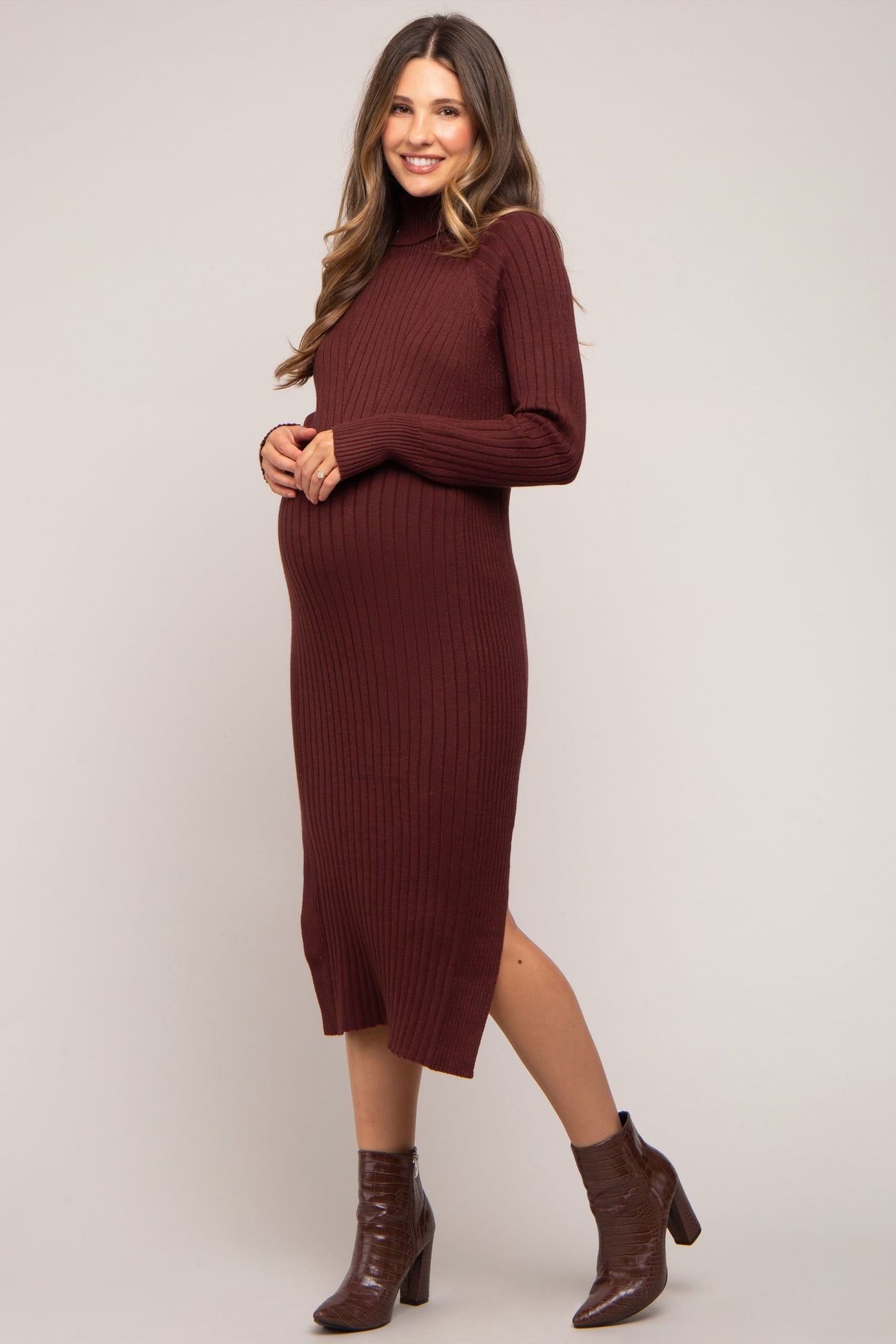 woman wearing a ribbed burgundy maternity dress with a turtleneck and side slits, showcasing her baby bump