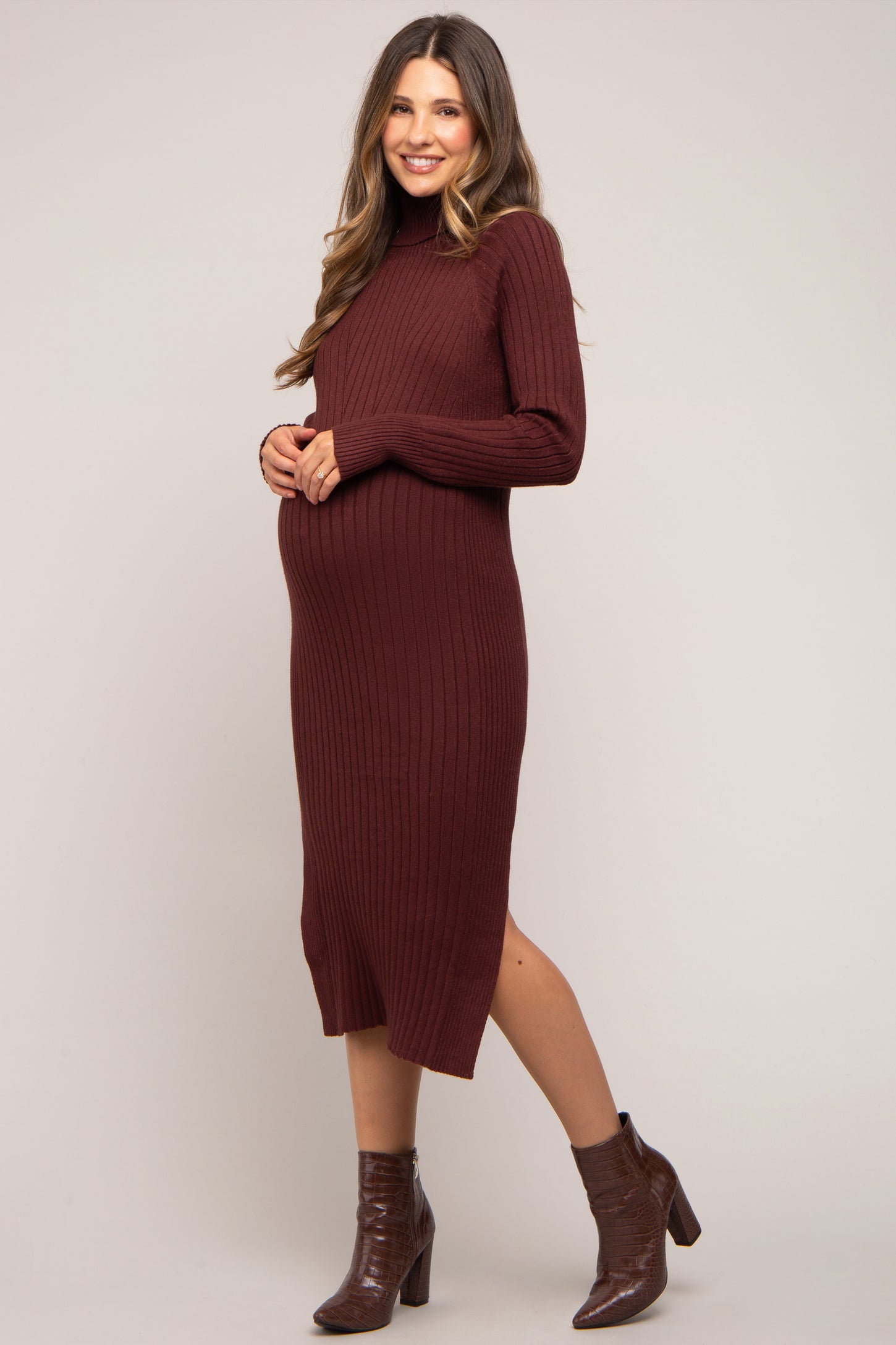 woman wearing a ribbed burgundy maternity dress with a turtleneck and side slits, showcasing her baby bump
