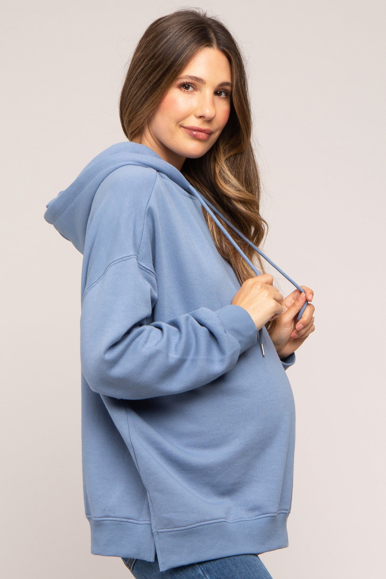 woman wearing a light blue maternity hoodie with a relaxed fit and drawstring hood, showing her baby bump