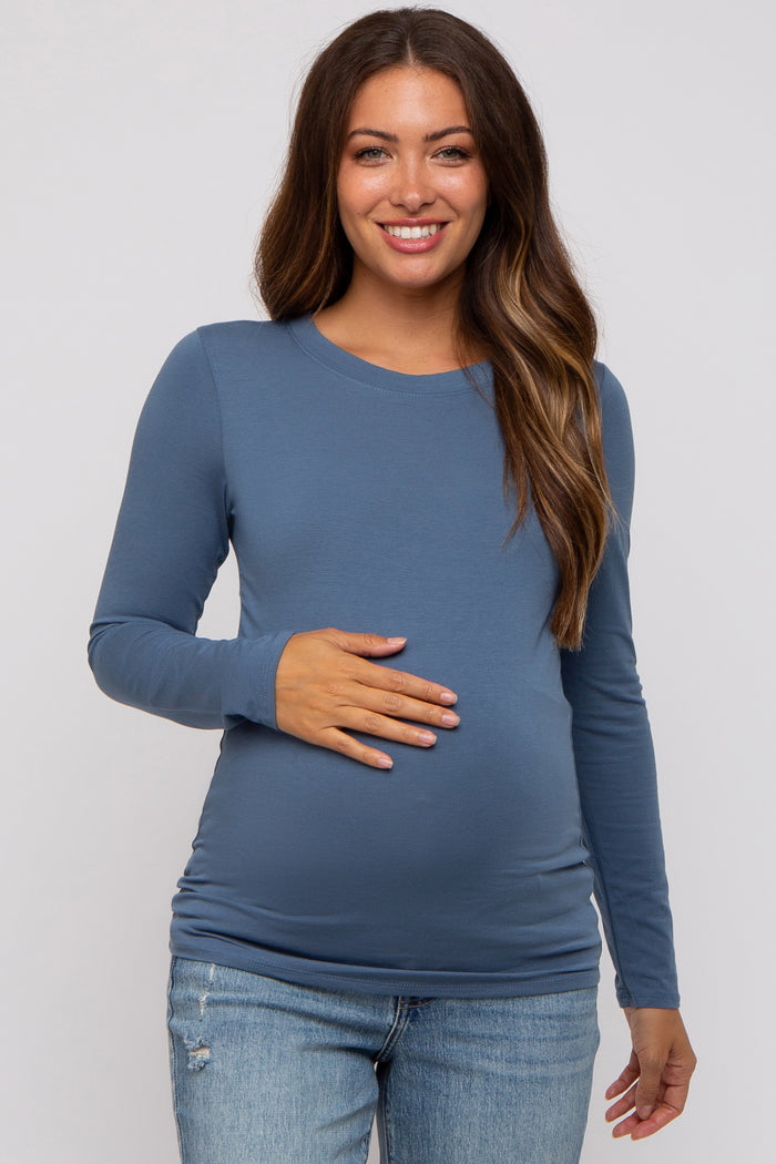 woman wearing a blue long sleeve maternity top and showing her baby bump while smiling