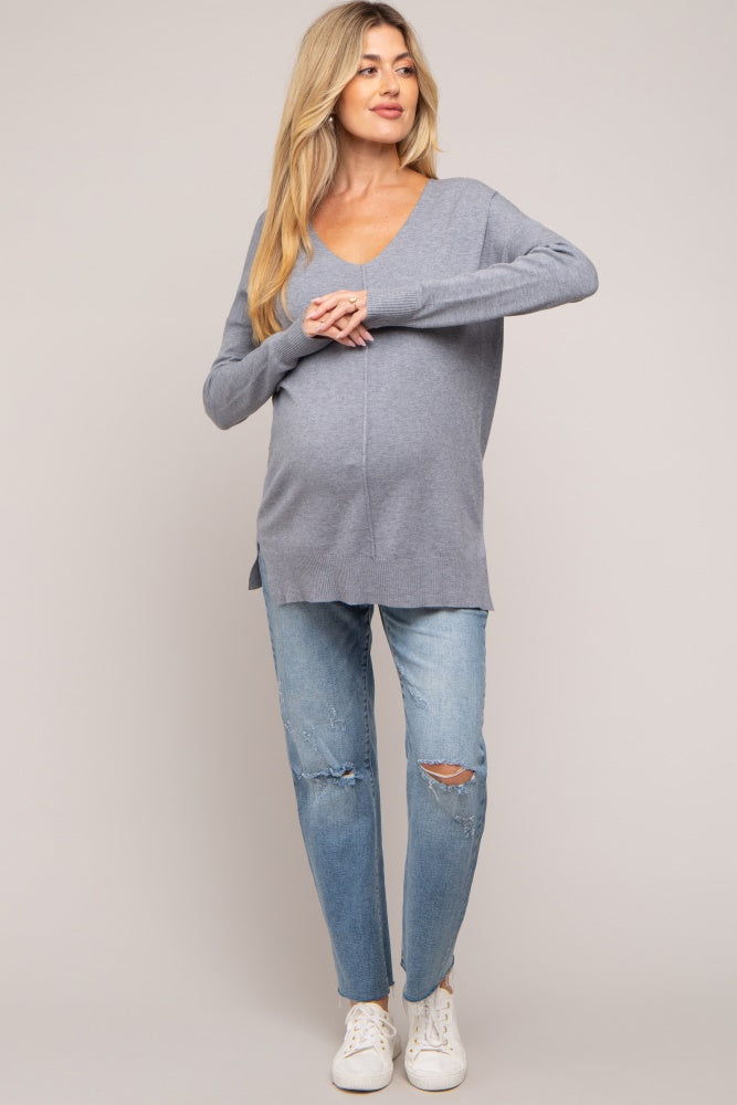 woman wearing a grey v-neck maternity sweater and distressed jeans, showing her baby bump