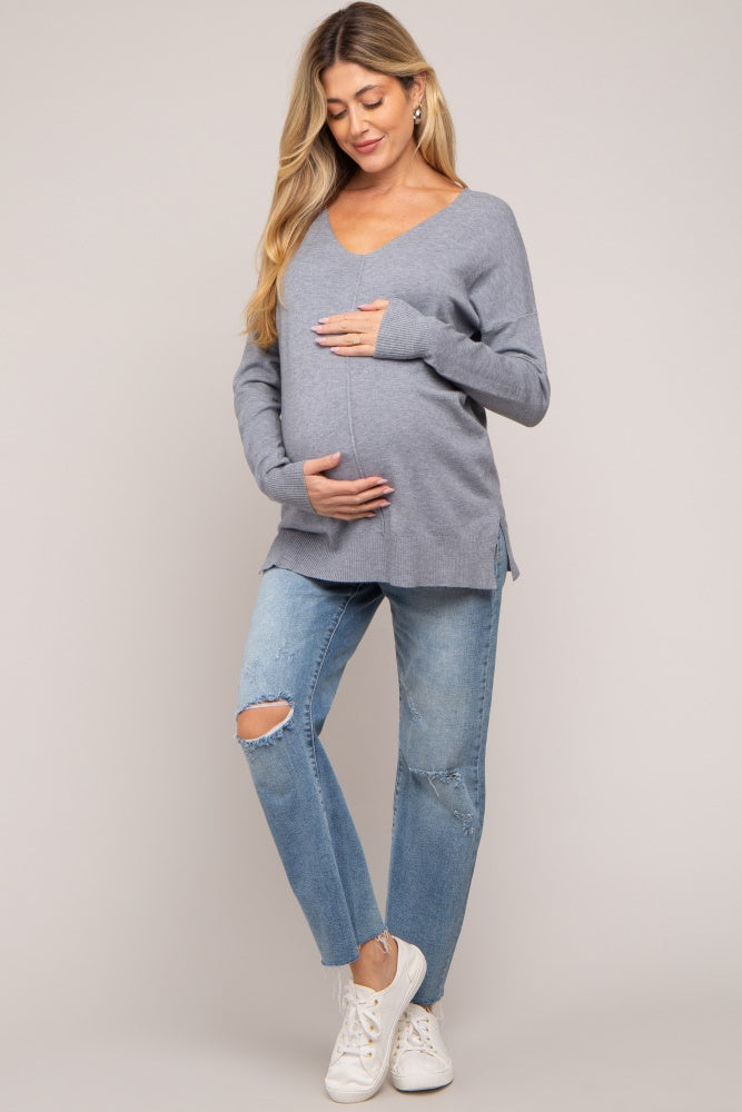 woman wearing a grey maternity sweater with a v-neck and light blue ripped jeans, showing her baby bump