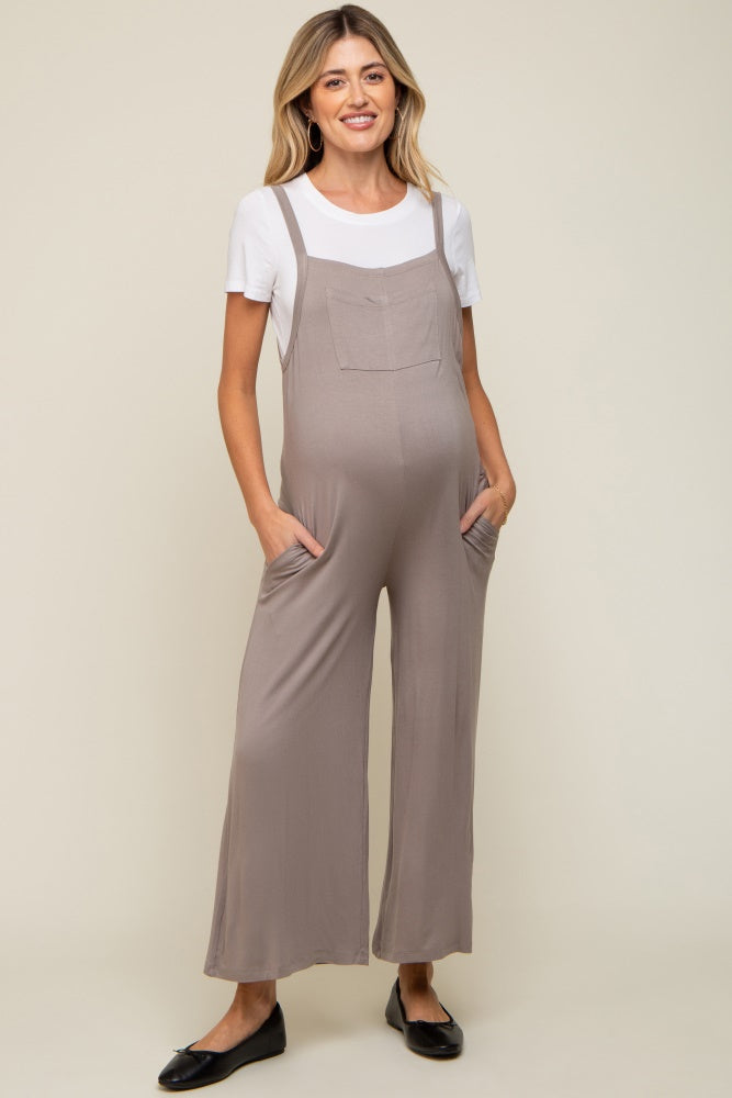 woman wearing a light brown maternity jumpsuit with pockets over a white t-shirt and showing a baby bump