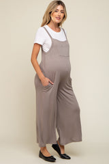 woman wearing a beige maternity jumpsuit with side pockets over a white t-shirt and showing her baby bump