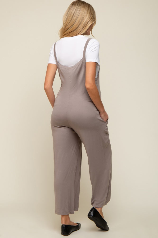 woman wearing a light gray maternity jumpsuit with adjustable straps and side pockets, viewed from the back