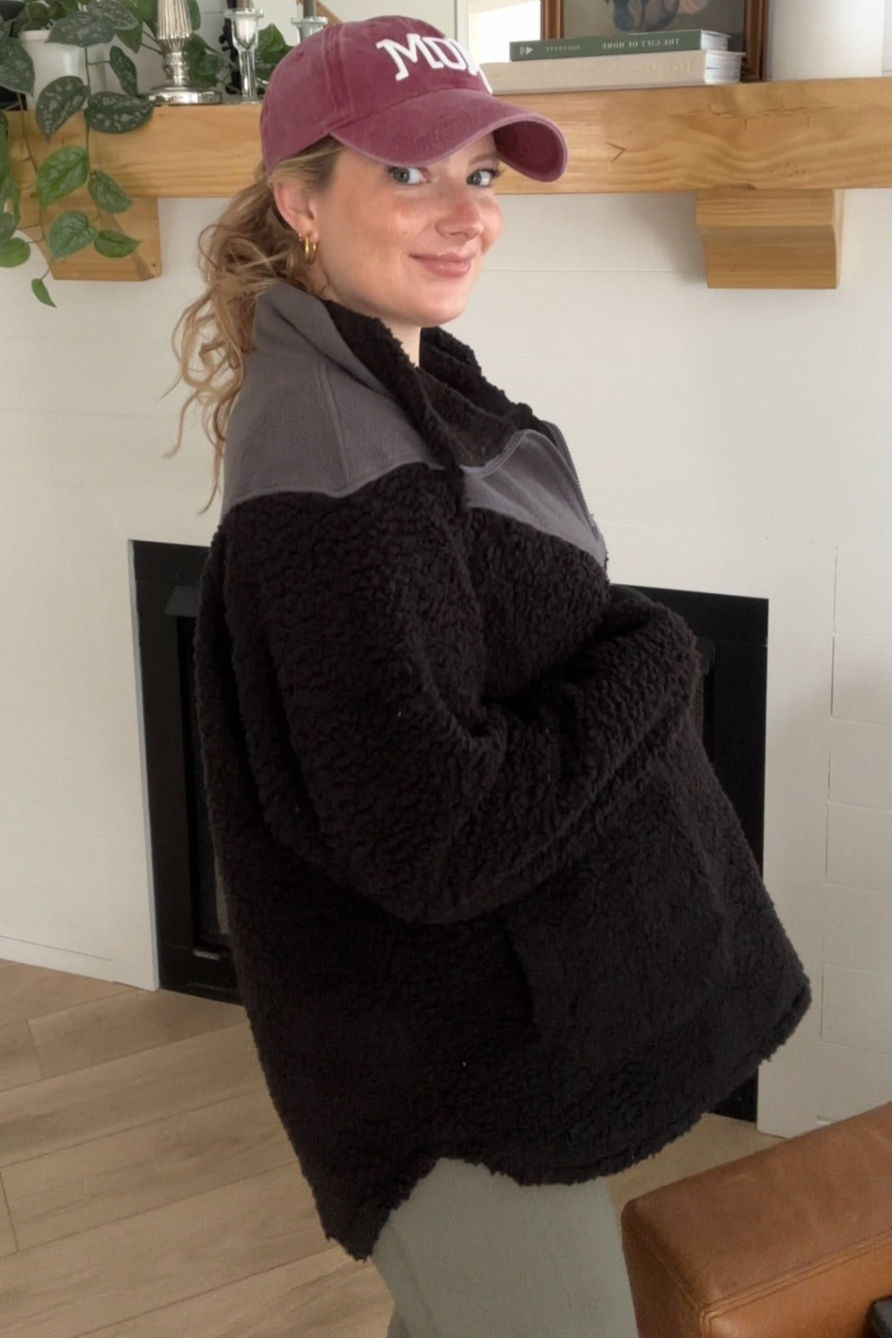 woman wearing a black and gray fleece maternity pullover with a baby bump, styled with a baseball cap
