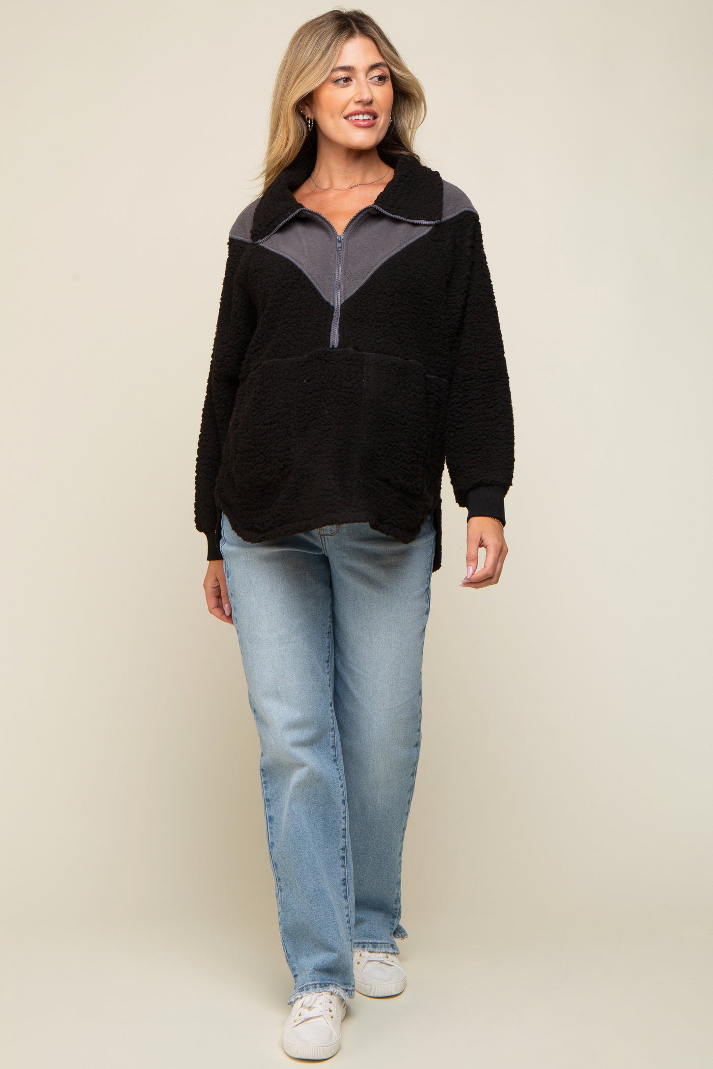 woman wearing a black and gray color block half zip maternity pullover with a relaxed fit and blue jeans