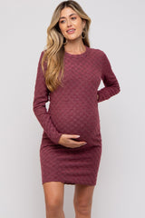 woman wearing a maroon long sleeve maternity dress with textured pattern and holding her baby bump