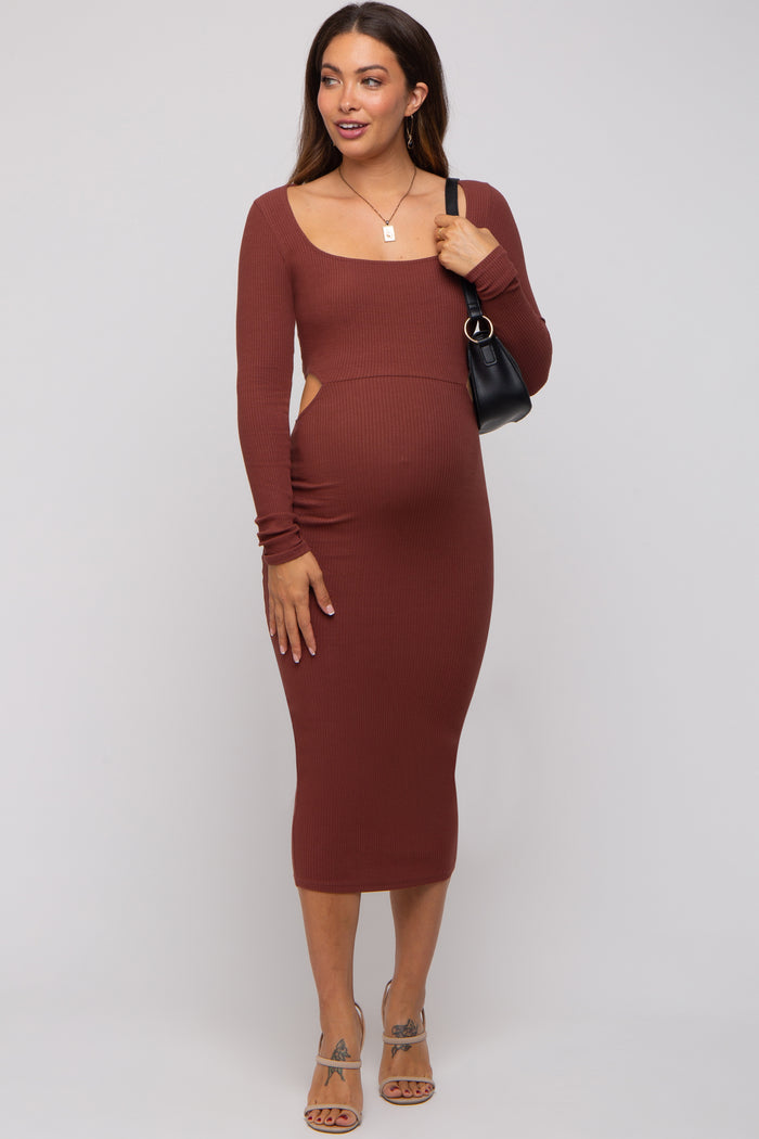 woman wearing a rust ribbed long sleeve maternity dress with cutouts and a visible baby bump, holding a black bag
