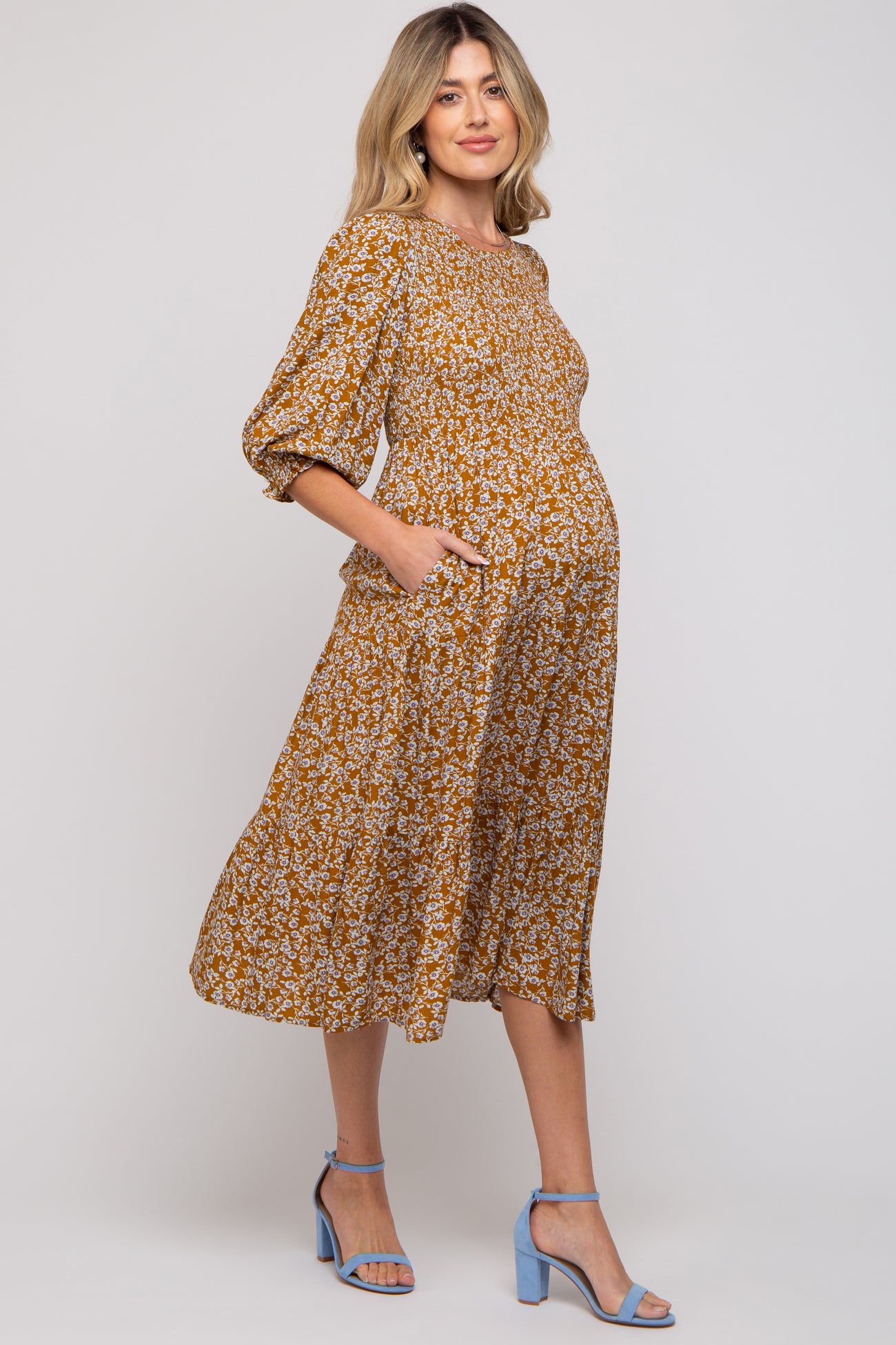 woman wearing a mustard floral midi maternity dress with pockets and a visible baby bump