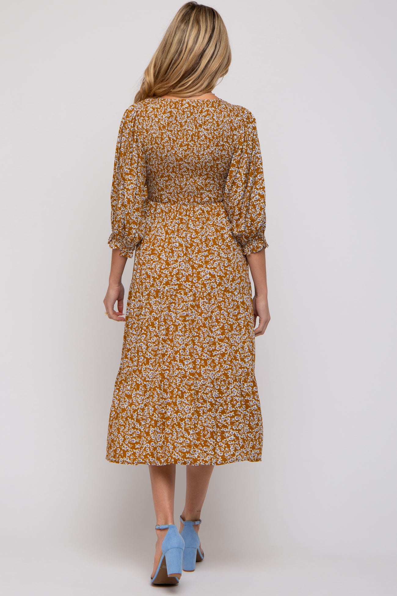 woman wearing a floral print mustard maternity dress with three-quarter puff sleeves and a midi length from the back