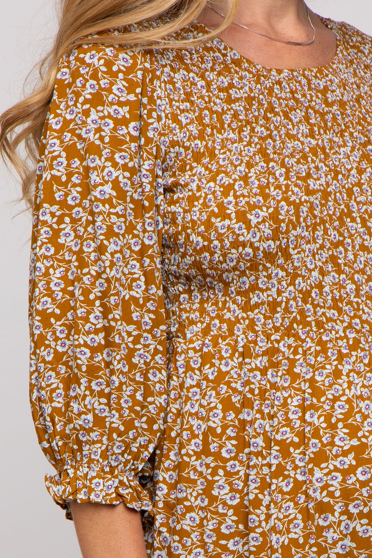 close-up of a woman wearing a smocked mustard floral maternity top with three-quarter sleeves