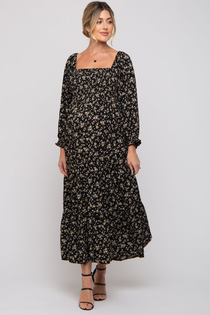 woman wearing a black floral maternity dress with long sleeves and a square neckline, featuring a flowing skirt and visible baby bump
