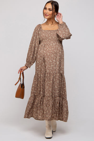 woman wearing a brown floral maternity maxi dress with puff sleeves and tiered skirt, holding a handbag