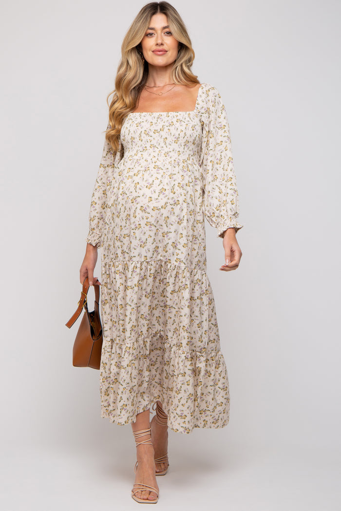 woman wearing a light floral maternity dress with a square neckline and tiered skirt, holding a brown handbag and showing baby bump