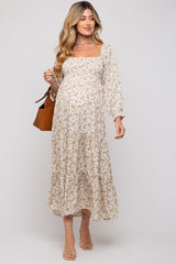 woman wearing a floral print maternity dress with a square neckline and long sleeves, holding a brown handbag and showing her baby bump