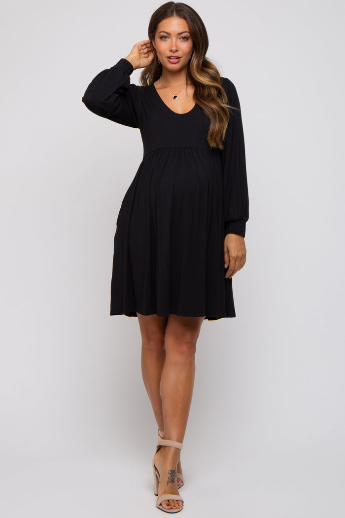 woman wearing a black long sleeve maternity dress with a v-neck and flowing skirt, highlighting her baby bump