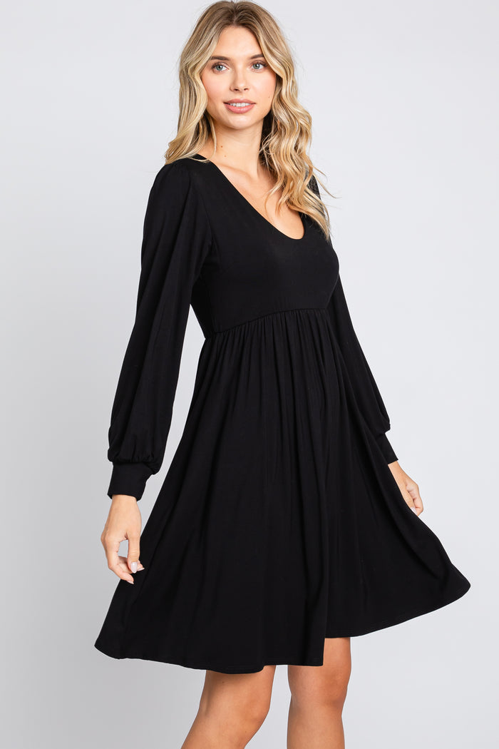 woman wearing a black long sleeve A-line dress with a V-neck and gathered waist, posing with a twirl