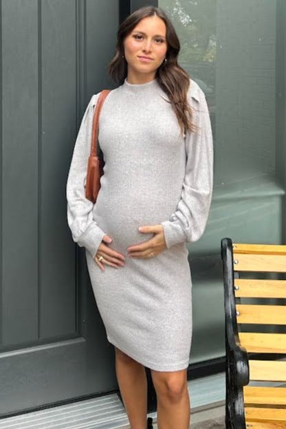 woman wearing a light gray long sleeve sweater dress, showing her baby bump while holding it gently