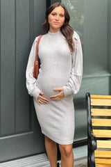 woman wearing a light gray long sleeve sweater dress, showing her baby bump while holding it gently