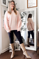 woman wearing a soft pink oversized sweater with balloon sleeves, paired with black leggings and beige knee-high boots