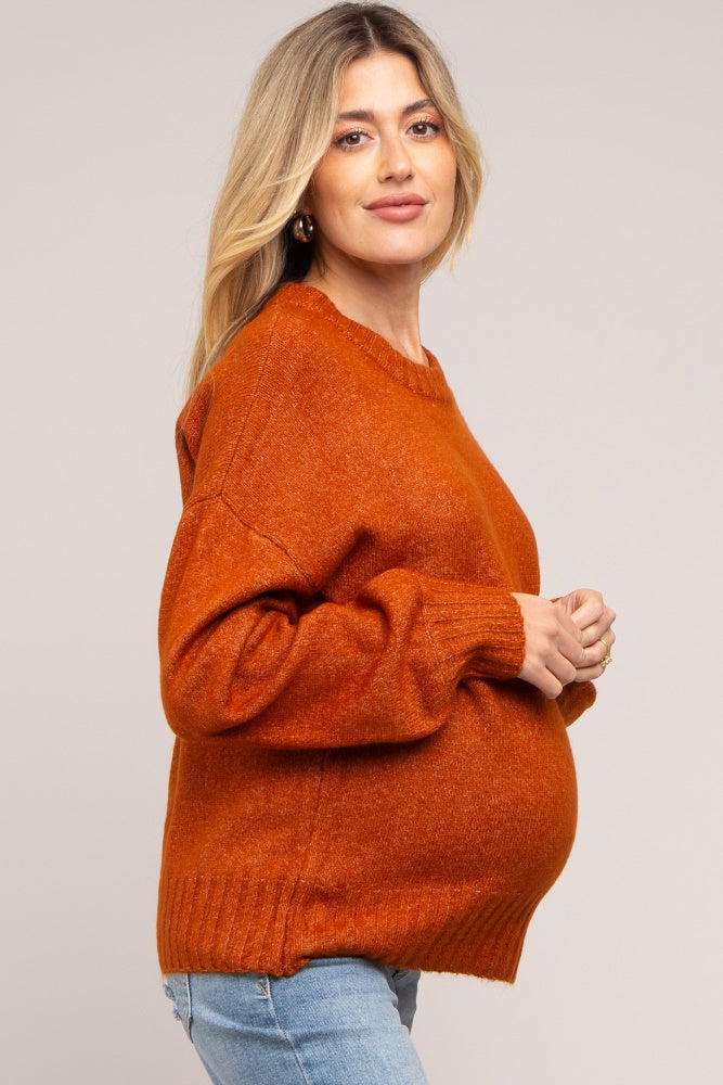 woman wearing a rust-colored oversized maternity sweater and showing her baby bump