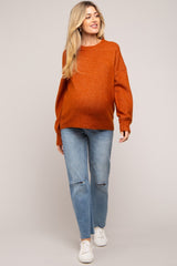 woman wearing an orange oversized maternity sweater and distressed jeans, showcasing her baby bump