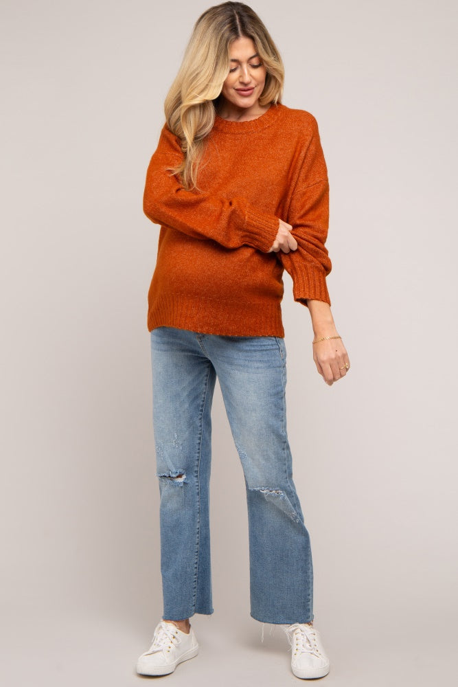 woman wearing an orange maternity sweater and distressed light blue jeans, showing her baby bump