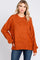 woman wearing an orange oversized sweater with a round neckline and relaxed fit, paired with blue jeans
