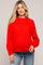 woman wearing a bright red maternity sweater with a relaxed fit, holding her baby bump, paired with blue jeans