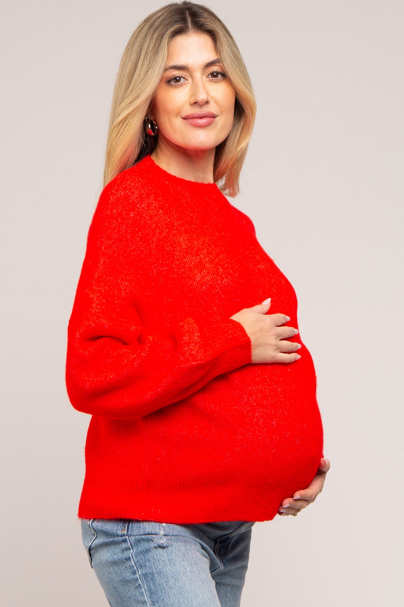 woman wearing a bright red maternity sweater and showing her baby bump while posing with a smile