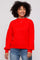 woman wearing a bright red cozy oversized sweater and blue jeans with a smile on her face