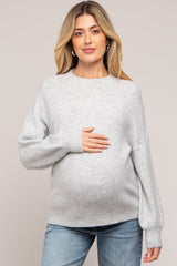 woman wearing a light gray maternity sweater and holding her baby bump
