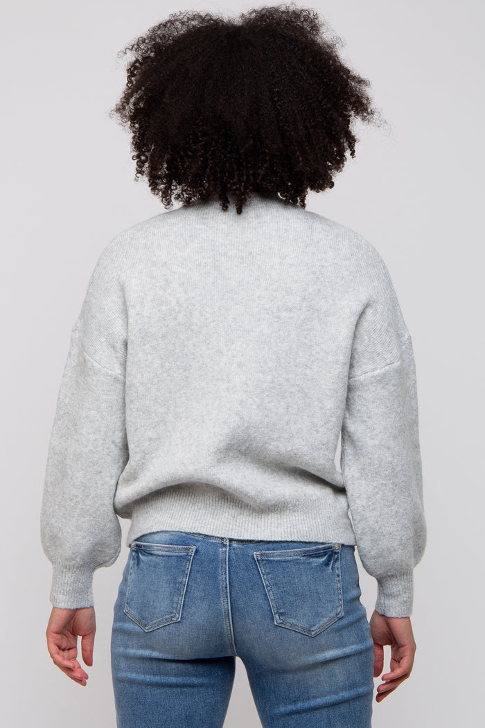 woman wearing a light gray oversized sweater with puff sleeves, viewed from the back, paired with blue jeans