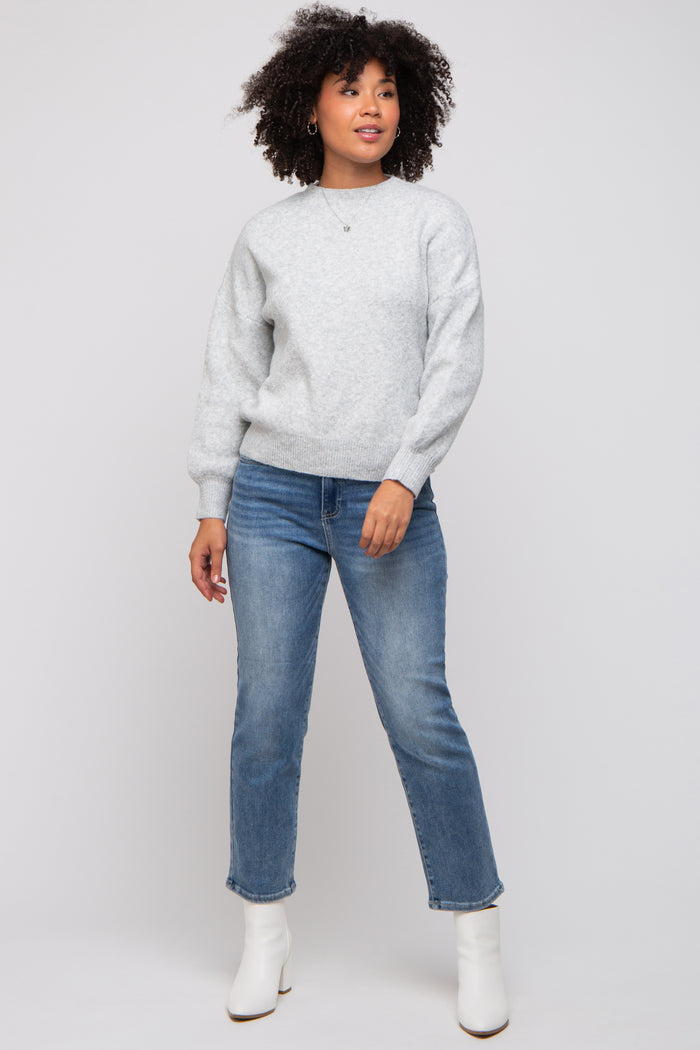woman wearing a light gray sweater and blue jeans, standing and posing with curly hair and white ankle boots