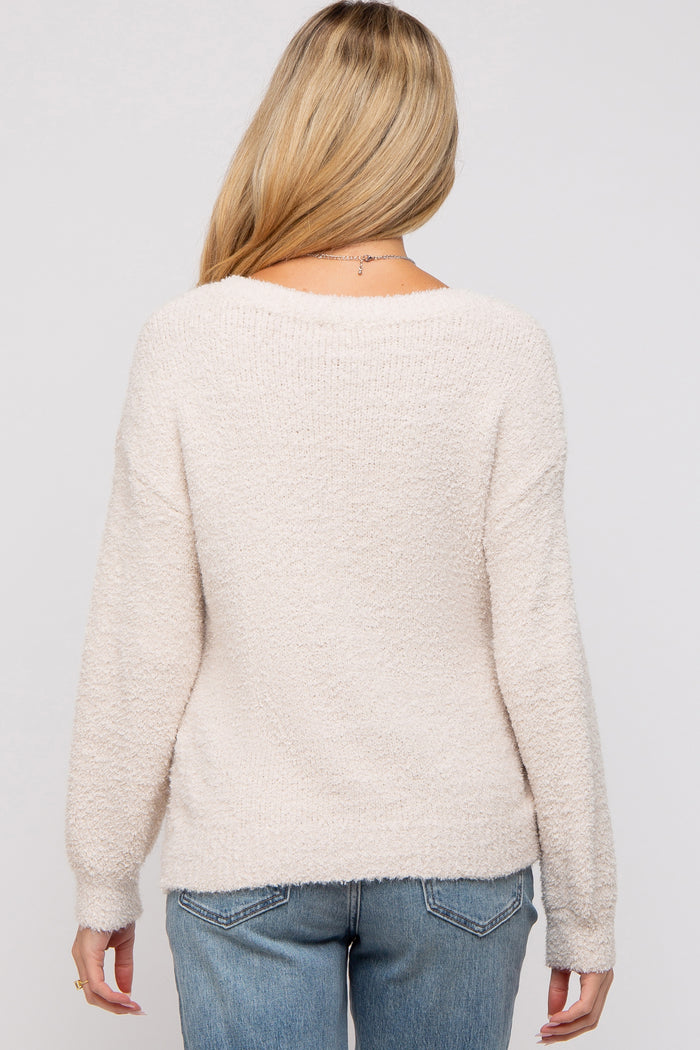 woman wearing a light beige maternity sweater with a soft texture, viewed from the back, paired with blue jeans