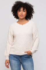 woman wearing a cream-colored textured sweater with long sleeves and relaxed fit, paired with blue jeans