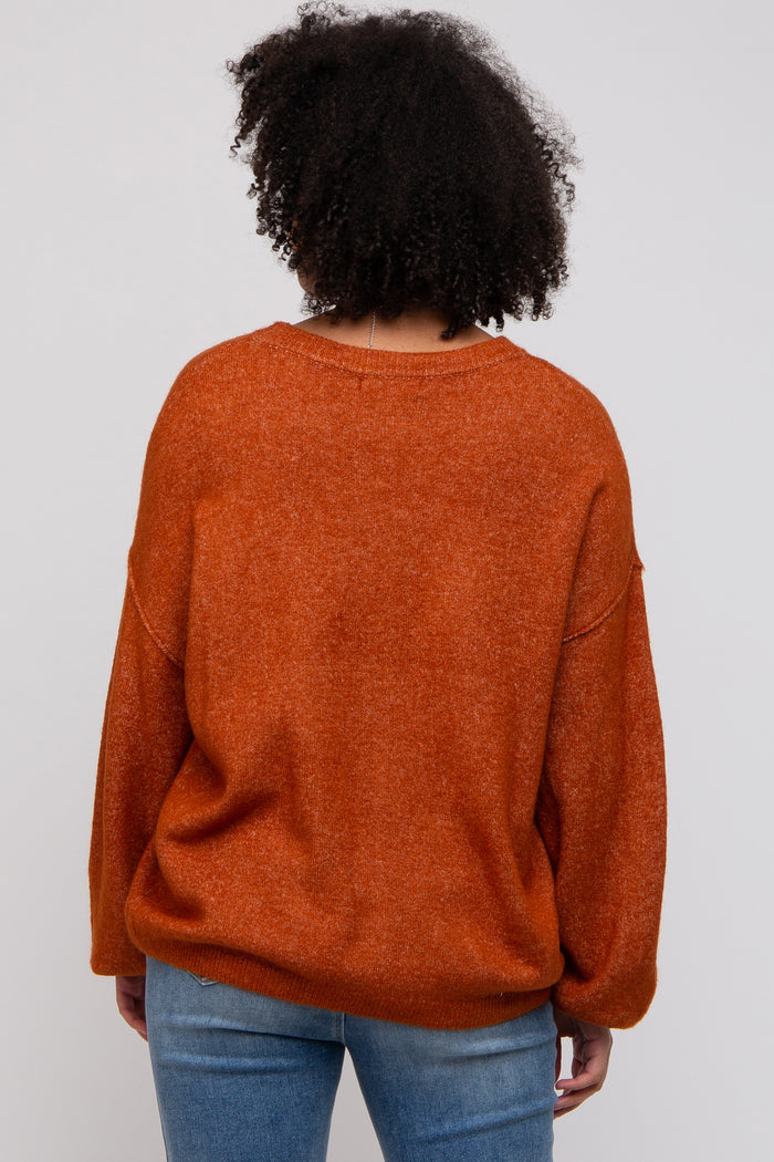woman wearing an oversized orange sweater with a relaxed fit and long sleeves, viewed from the back